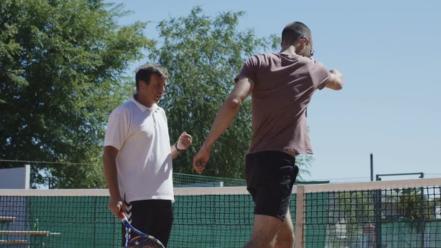 Side view of coach and trainee with tennis rackets standing on court in sunlight and having practice in team