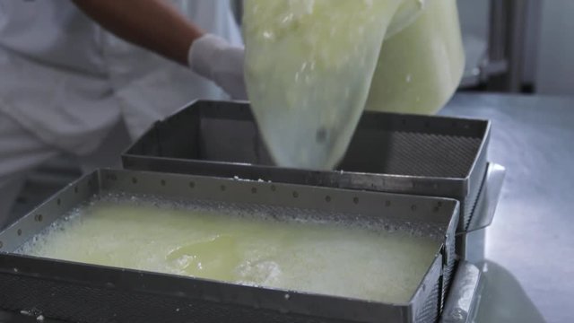 Factory curd making process. Caucasian adult man farmworker in white uniform with latex gloves separates milk whey from curd at modern farm factory in slow motion.