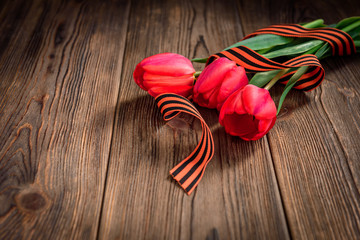 St. George ribbon, red tulips and paper greeting card on wooden background. Victory day or Fatherland defender day.