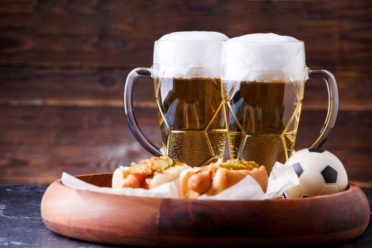 Photo of two mugs of beer and hot dogs on wooden tray with football