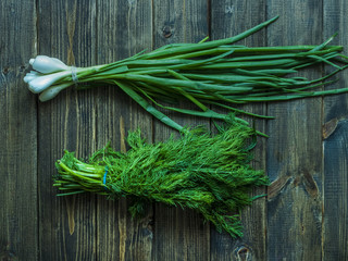 bunch of green onion and dill on a wooden surface