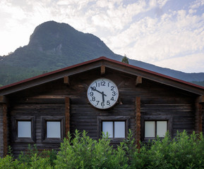 Fototapeta na wymiar Large clock on small wooden building in front of tall mountain at time of 5:50 in the afternoon