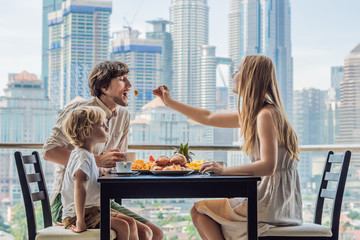 Happy family having breakfast on the balcony. Breakfast table with coffee fruit and bread croisant on a balcony against the backdrop of the big city