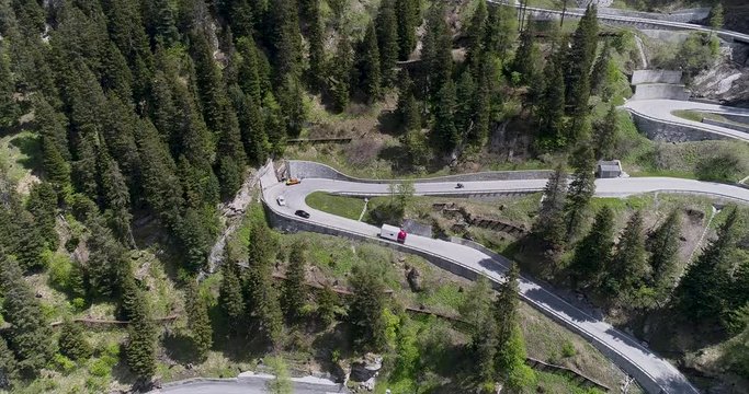 Aerial view of mountain serpentine road with trucks and cars driving on zig zag go up and down in Europe Switzerland 4K