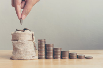 Hand of male or female putting coins in money bag with coin stack step growing growth saving money,...