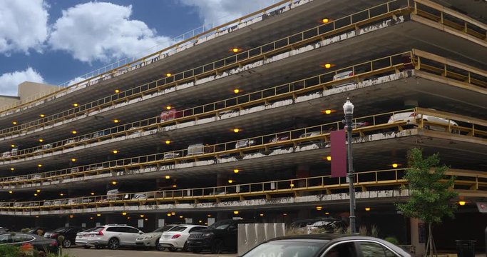 A daytime exterior (DX) establishing shot of a large parking garage in the business district of a large city.  	