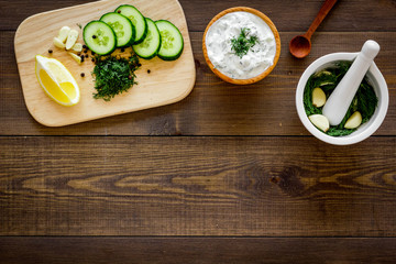 Greek yogurt as salad dressing. Bowl with yogurt, greenery, cucumber, oranges on cutting board on dark wooden kitchen desk top view space for text