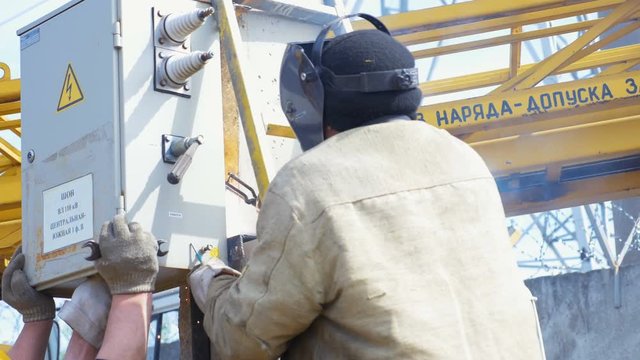 person holds switchgear and man fixes equipment doing welding