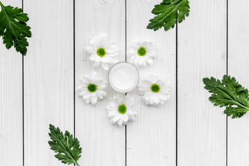 Moisturizing cream based of natural herbal ingredients. Chamomile cream in small jar near chamomile flowers on white background top view copy space pattern