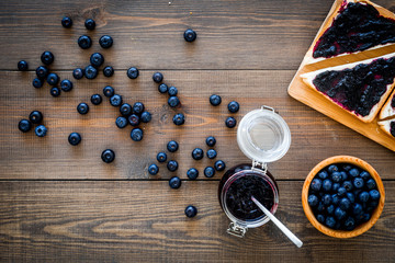 Sandwiches with blueberry jam for breakfast on dark wooden background top view copy space