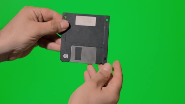 A hand opening a floppy disk over a green background.
