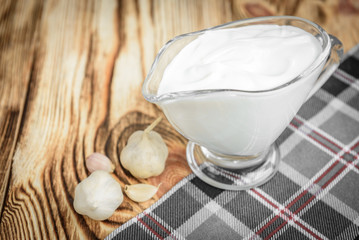 Gravy boat with sour cream and garlic on wooden background.