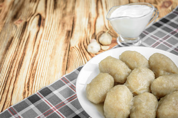 Potato dumplings with stuffed minced meat on a white plate and gravy boat with sour cream on wooden background.