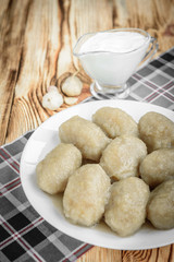 Potato dumplings with stuffed minced meat on a white plate and gravy boat with sour cream on wooden background.