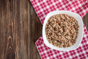Boiled buckwheat in white bowl on dark wooden table.