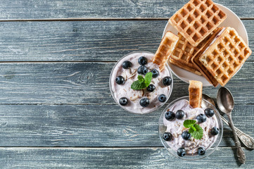 Cottage cheese dessert with blueberries in a glass cup and homemade Viennese waffles on a wooden background. Top view. Copy space