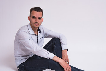 Portrait of a cute young man sitting on the floor on a white background