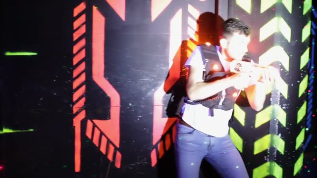 Group of young people having fun on dark lasertag arena in colorful beams of laser guns