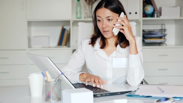 Practicioner woman in medical uniform talking by phone at  laptop  in clinic