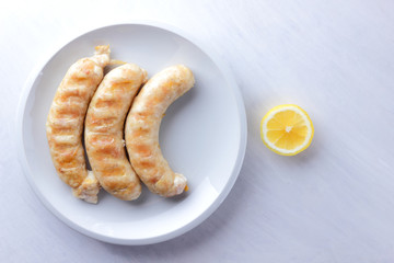 Grilled sausages on white background, chicken sausages on a white plate, meat dish with lemon, copy space, delicious fast food, American cuisine
