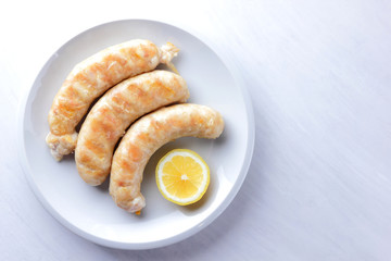 Grilled sausages on white background, chicken sausages on a white plate, meat dish with lemon, copy space, delicious fast food, American cuisine