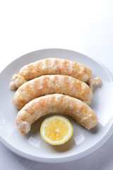 Grilled sausages on white background, chicken sausages on a white plate, meat dish with lemon, copy space, delicious fast food, American cuisine