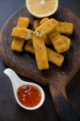 Close-up of fried fish sticks or breaded fish fillet with sauce and lemon, vertical shot