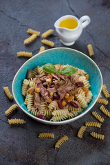 Tuna fillet with fusilli pasta served in a blue bowl, studio shot on a weathered asphalt background