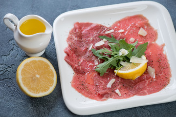 Carpaccio made of raw marbled beef and served with fresh arugula, parmesan cheese, lemon and olive oil, studio shot