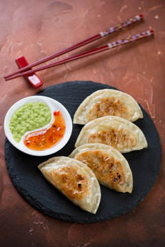 Stone slate with fried potstickers and dipping sauces on a rusty metal background, vertical shot