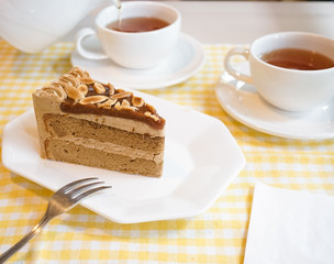 Afternoon tea. Sea salt caramel almond coffee cake serves with cup of teas. Blurred teapot is pouring tea on the background.