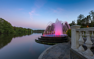 Fountain with illumination on the shore of the evening lake