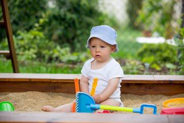 Little baby boy, playing in a sandpit with toys ..