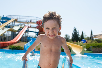 funny small caucasian kid in water park near cool azure swimming pool outdoor