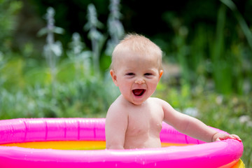 Cute little child, toddler boy, playing in small baby pool in backyard