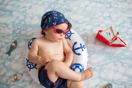 Cute toddler, baby boy sleeping on a tiny inflatable swim ring,  wearing swimsuit shorts and sunglasses