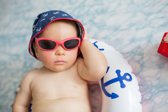 Cute toddler, baby boy sleeping on a tiny inflatable swim ring,  wearing swimsuit shorts and sunglasses