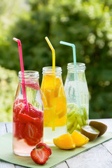 Trio of ice-cold fruit drinks on a wooden grey table on a summer garden background