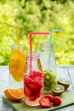 Trio of ice-cold fruit drinks on a wooden grey table on a summer garden background