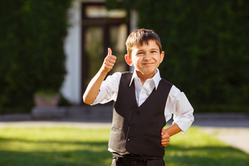 Cheerful boy in fashionable suit on green grass