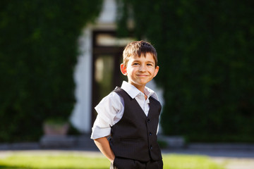 Cheerful boy in fashionable suit on green grass