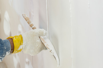 Hand with a spatula in the process of leveling the raw plaster. - obrazy, fototapety, plakaty