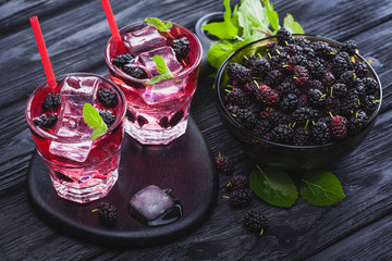 mulberry cocktail with ice and fresh mint on a black wooden table