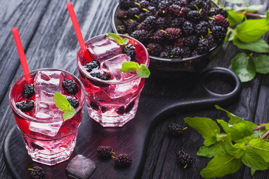 mulberry cocktail with ice and fresh mint on a black wooden table