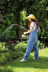 Hübsche rothaarige Frau steht in ihrem Garten und giesst Pflanzen mit einer Handbrause