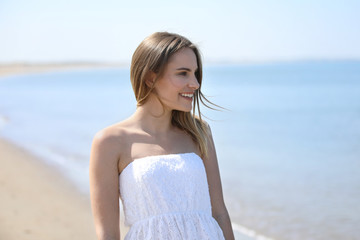 Fototapeta na wymiar Hübsche blonde Frau steht lachend am Meer und schaut auf das Wasser hinaus