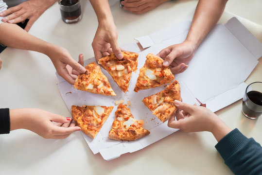 Image of teenage friends hands taking slices of pizza