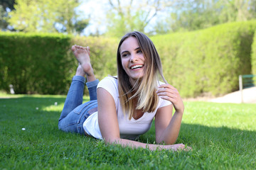 Hübsche blonde Frau liegt lachend und barfuß auf einem Rasen