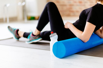 Fitness concept. Close up of woman relaxing after workout on the exercising mat..Portrait of Active Tired Woman Using Foam Roller in Light Room.