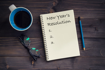 Notebook with 2019 New year's resolution massage, pencil, glasses and cup of coffee on wood background.